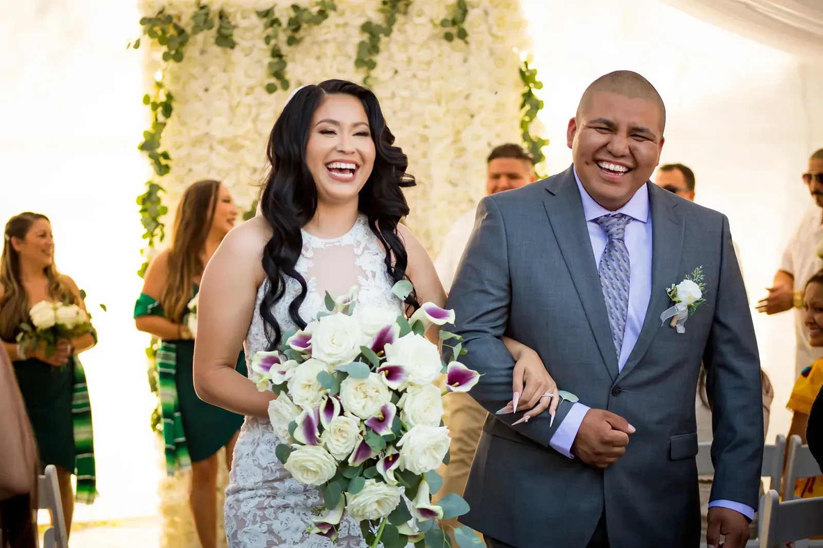 Newlyweds laughing arm in arm as they walk back up the aisle