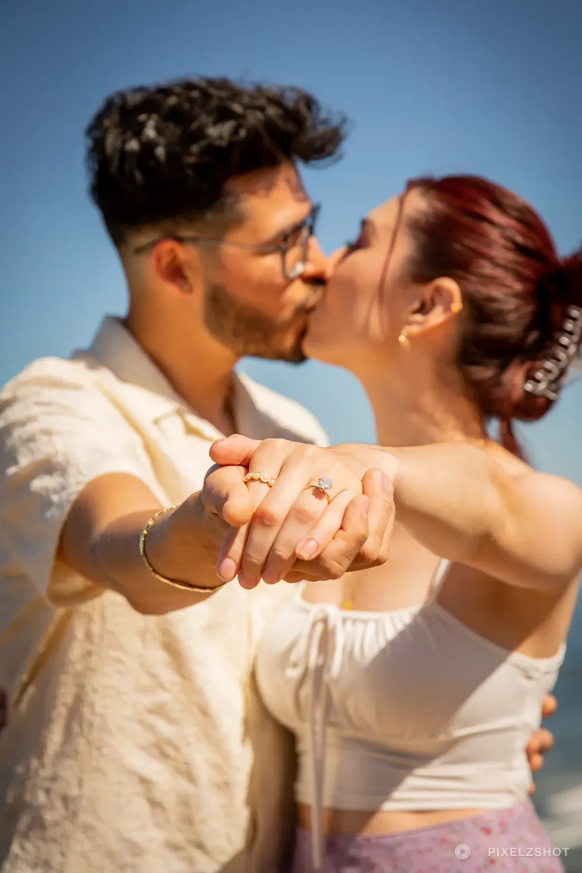 Danielle and Mathew kissing with their joined hands held out to the camera and the engagement ring in focus