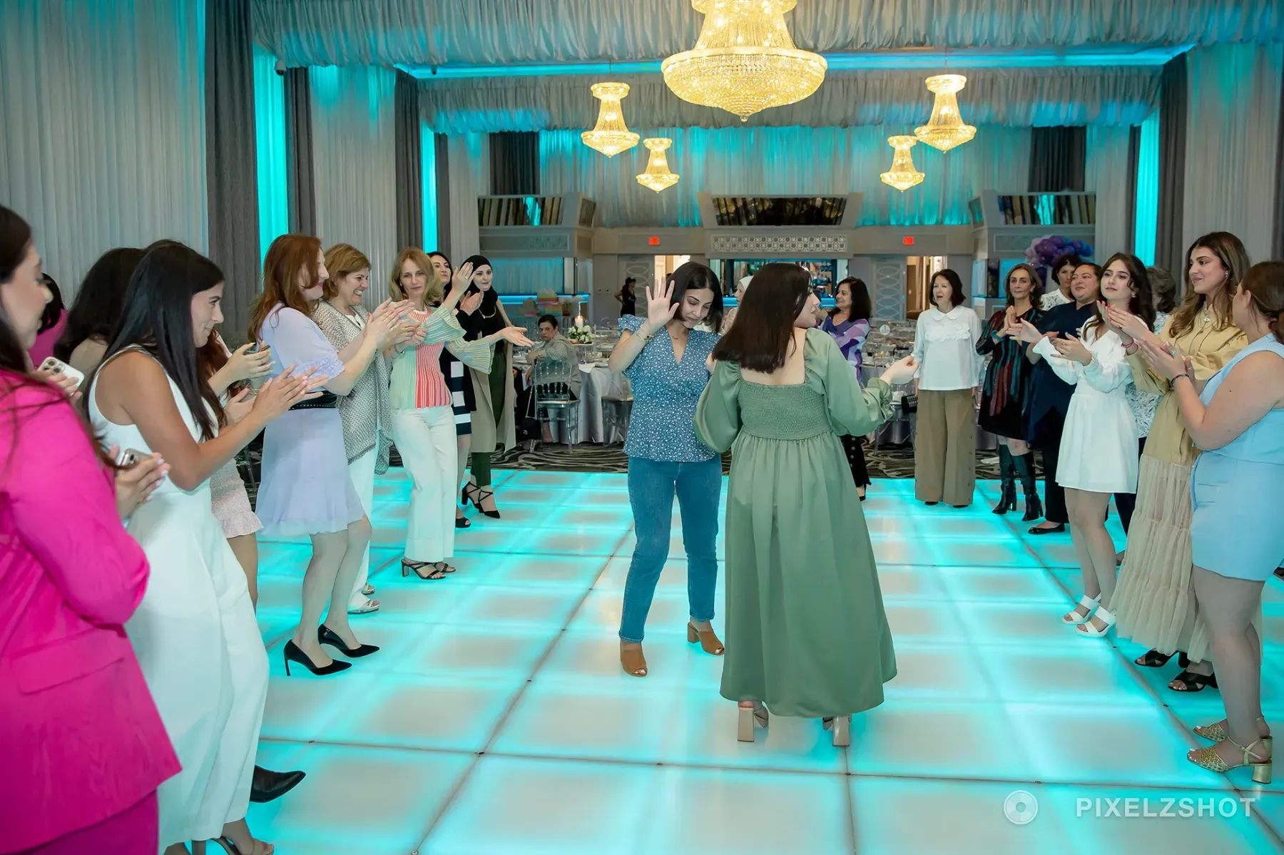 Two guests dancing in the middle of a wide circle on the lit dance floor, everyone else clapping them through it