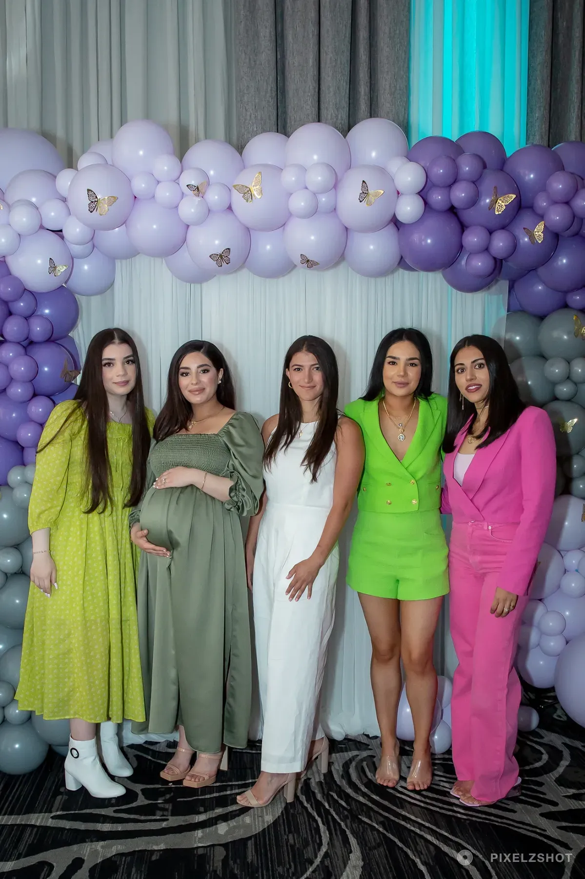 Alia lined up with four friends in front of the lilac and grey balloon garland, gold paper butterflies pinned through it