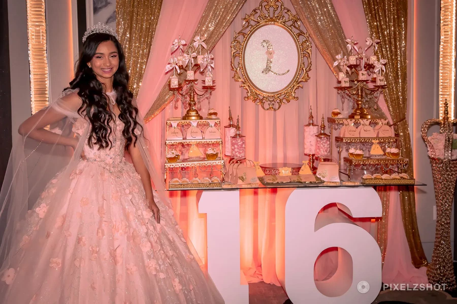 Lalaine in a blush ballgown and tiara beside her dessert table, under a gilded oval frame holding her initial
