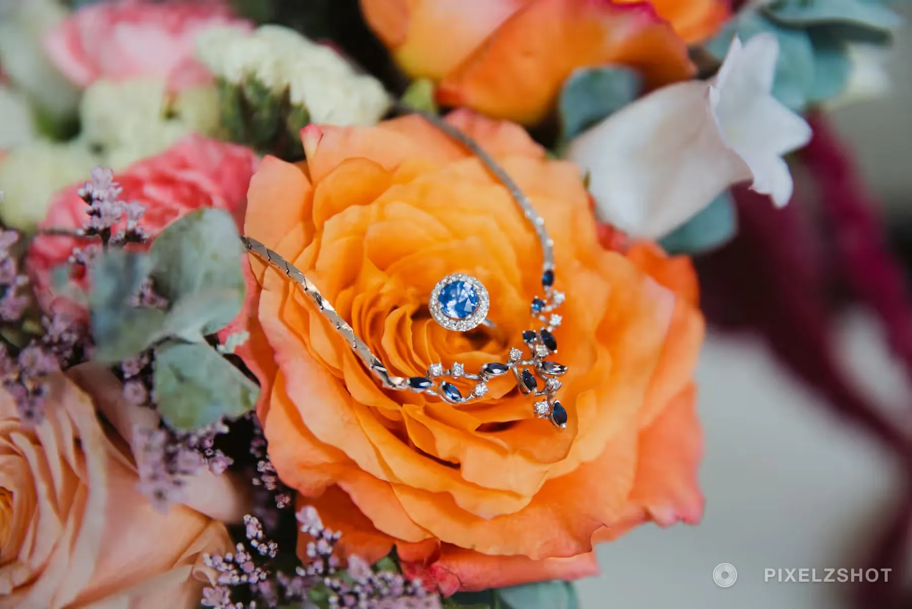 A sapphire and diamond ring and its matching necklace resting in the middle of an orange garden rose