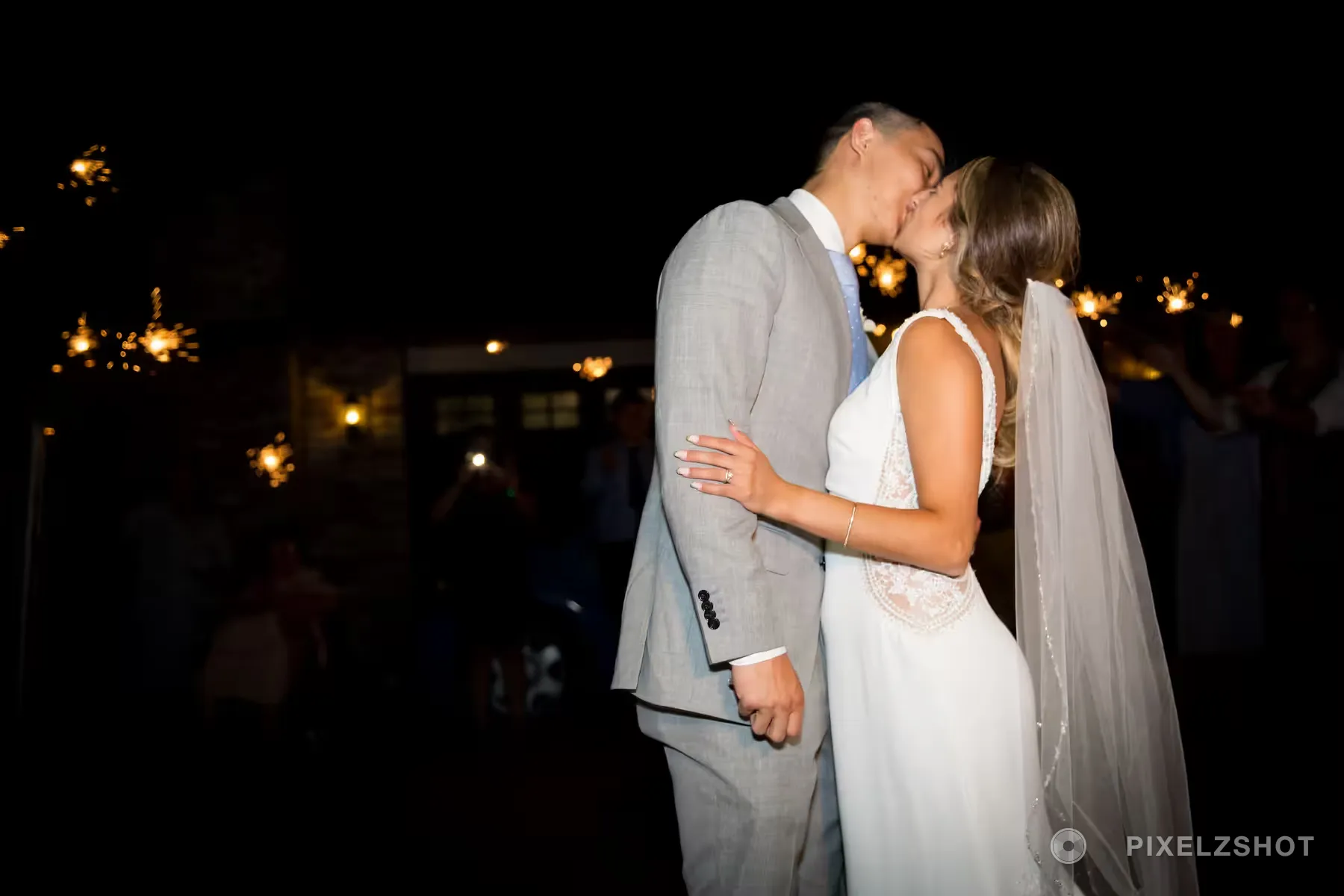 Caleb and Emily kissing outside after dark while guests hold lit sparklers around them