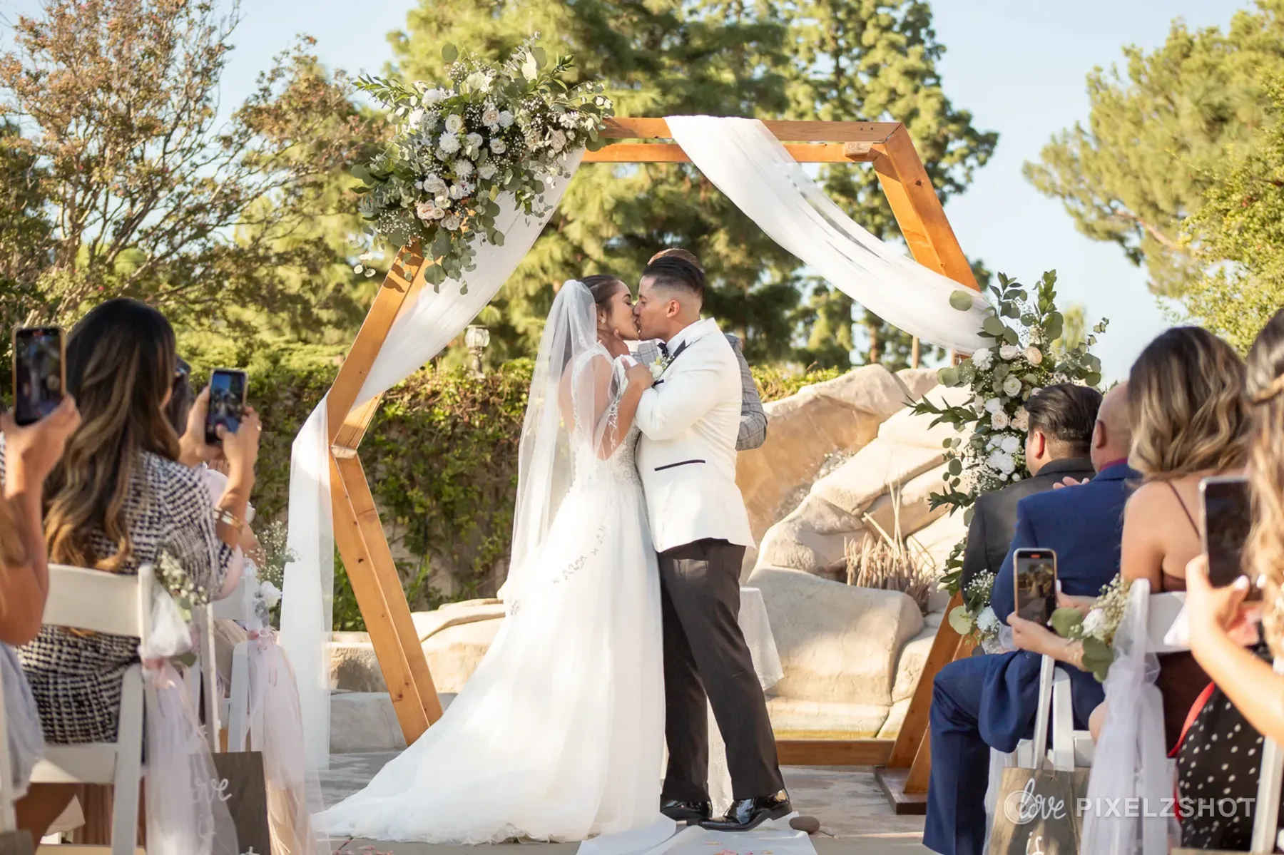 Leslie and Tito's first kiss beneath a draped wooden hexagon arch as guests raise their phones