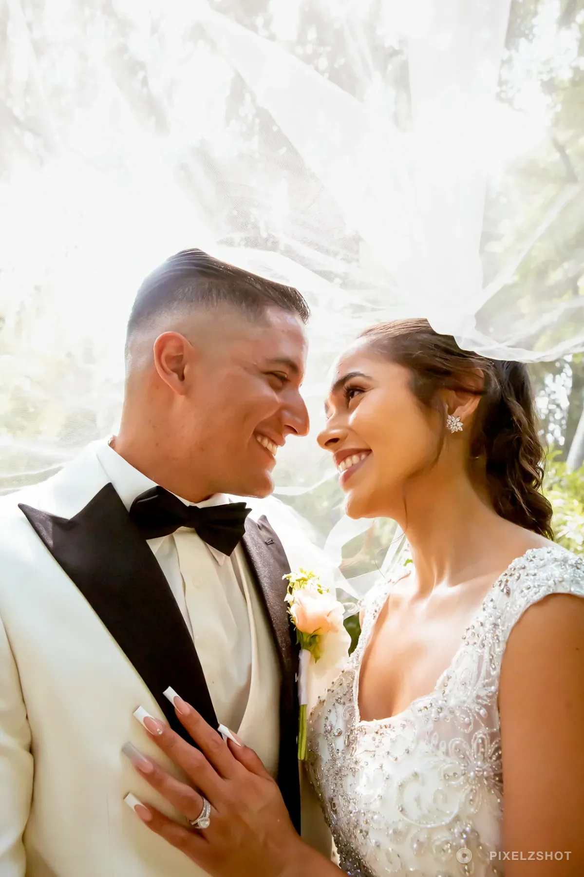 Leslie and Tito smiling at each other beneath her veil, backlit by afternoon sun