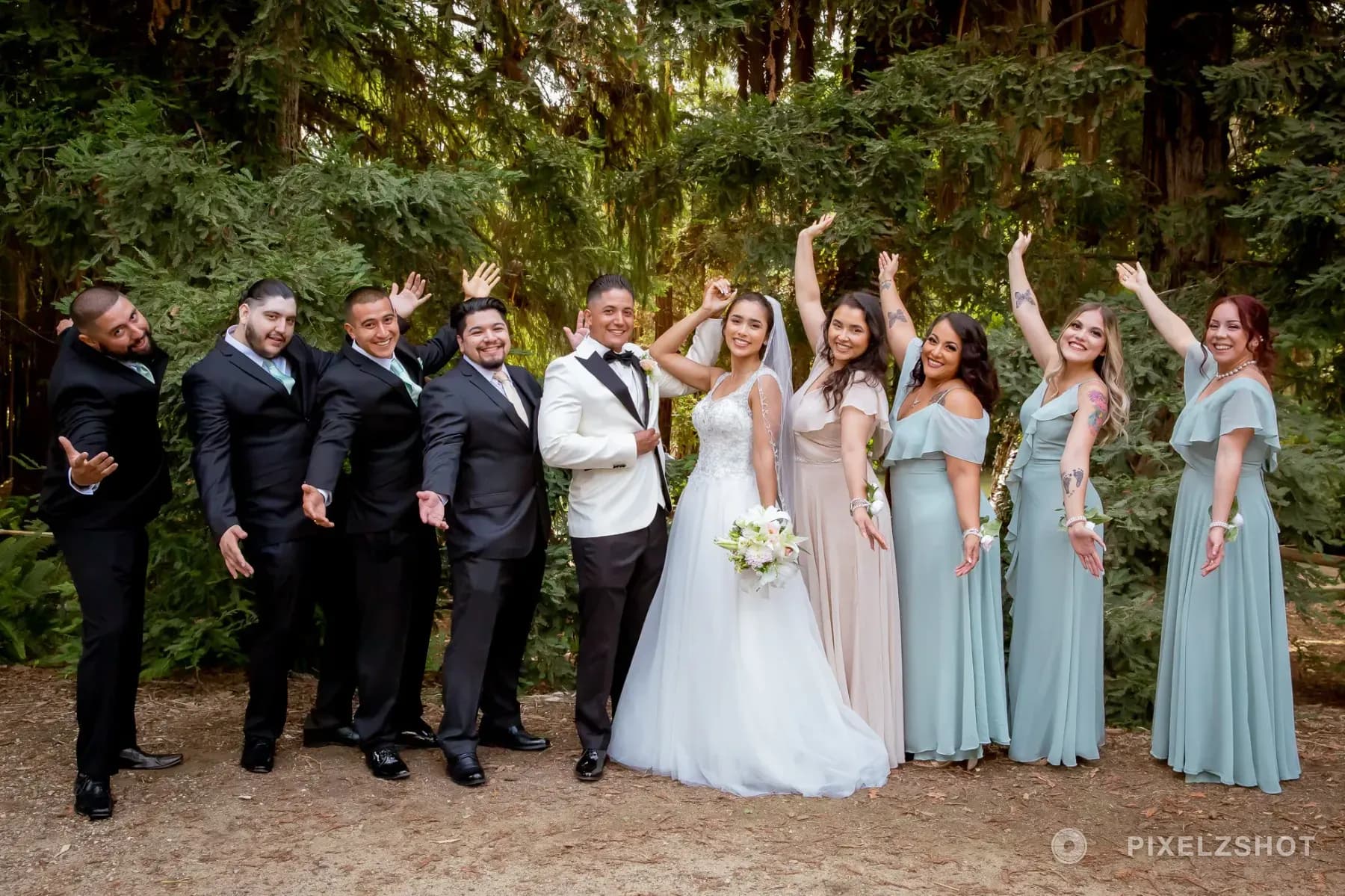 Leslie and Tito's wedding party cheering with arms raised in front of towering evergreens