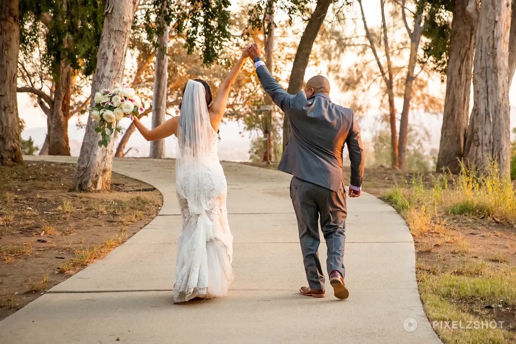 Natalie and Eduardo walking away down a Sylmar park path with their hands raised together in celebration