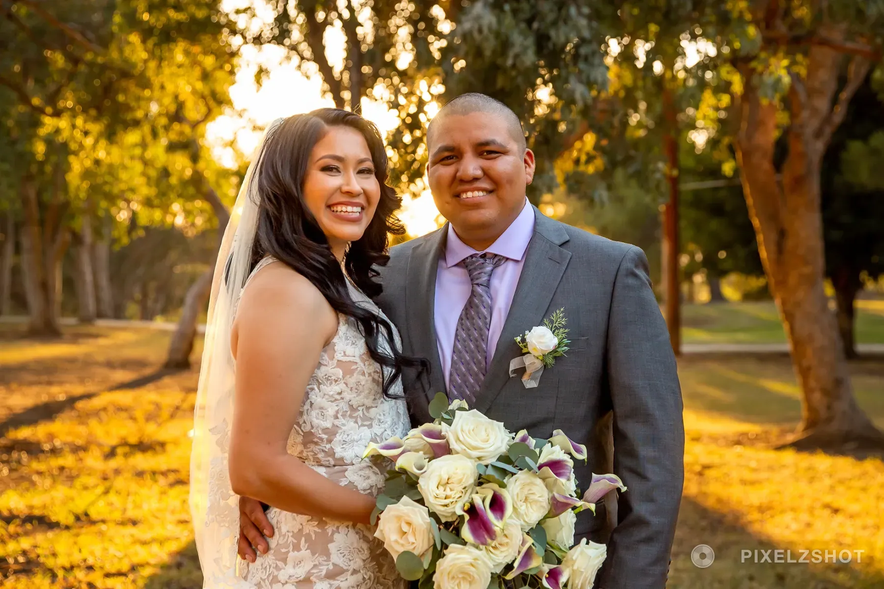 Natalie and Eduardo standing close together among eucalyptus trees in low golden sunlight