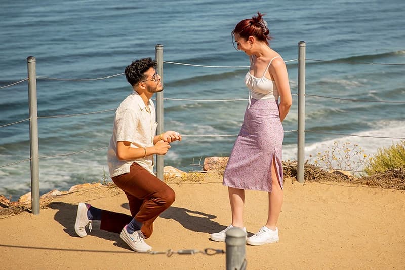 Man kneeling to propose on an oceanside cliff trail