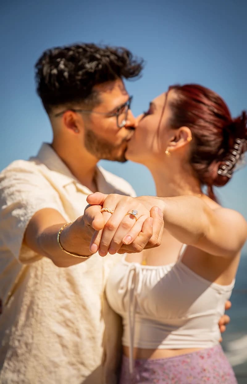 Close-up of a couple kissing on the beach, showing off her engagement ring
