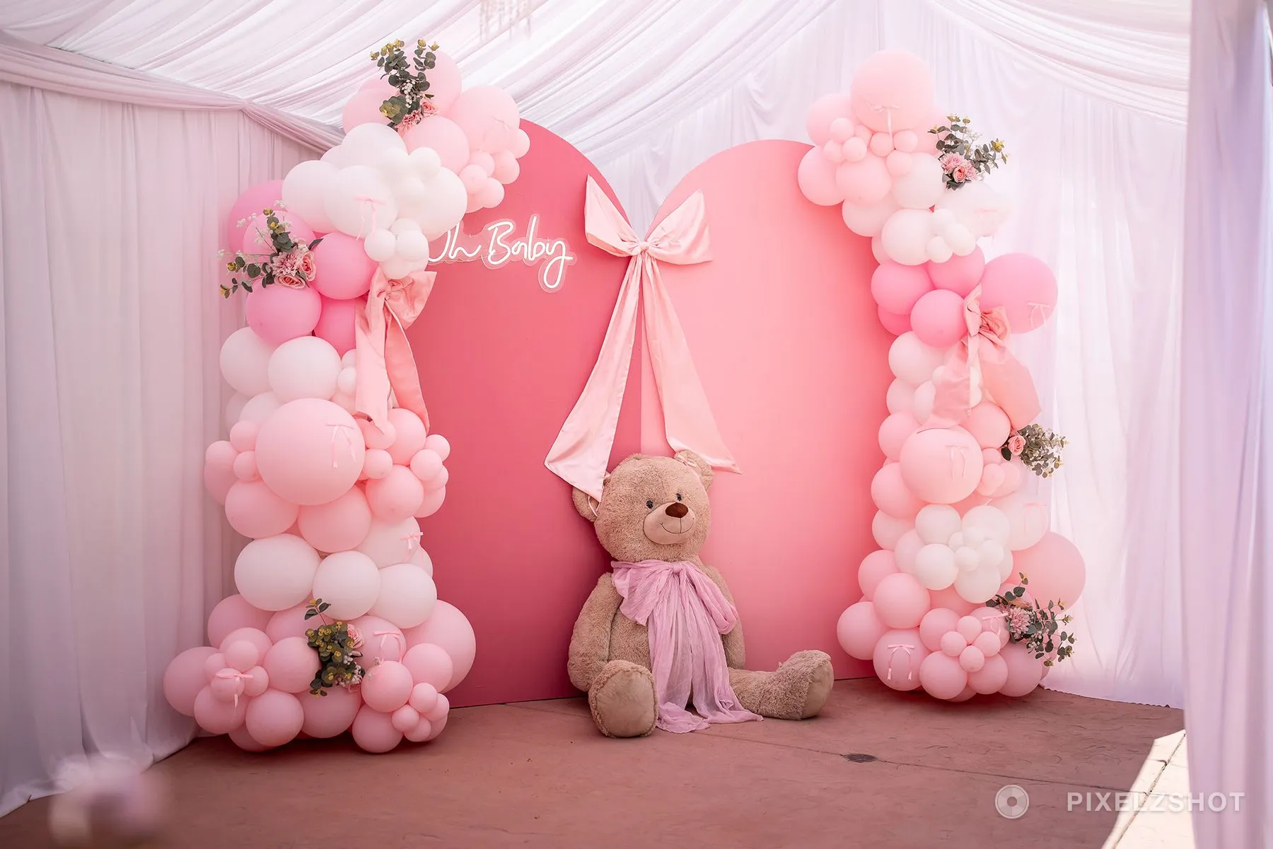 The backdrop before the guests arrived: two pink arches under an Oh Baby neon, balloon garlands down both sides, a satin bow, and a giant teddy bear at the foot of it
