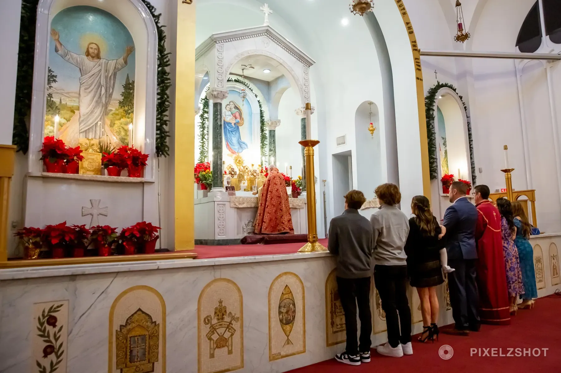 The family standing along the marble altar rail while the priest continues the service at the altar beyond
