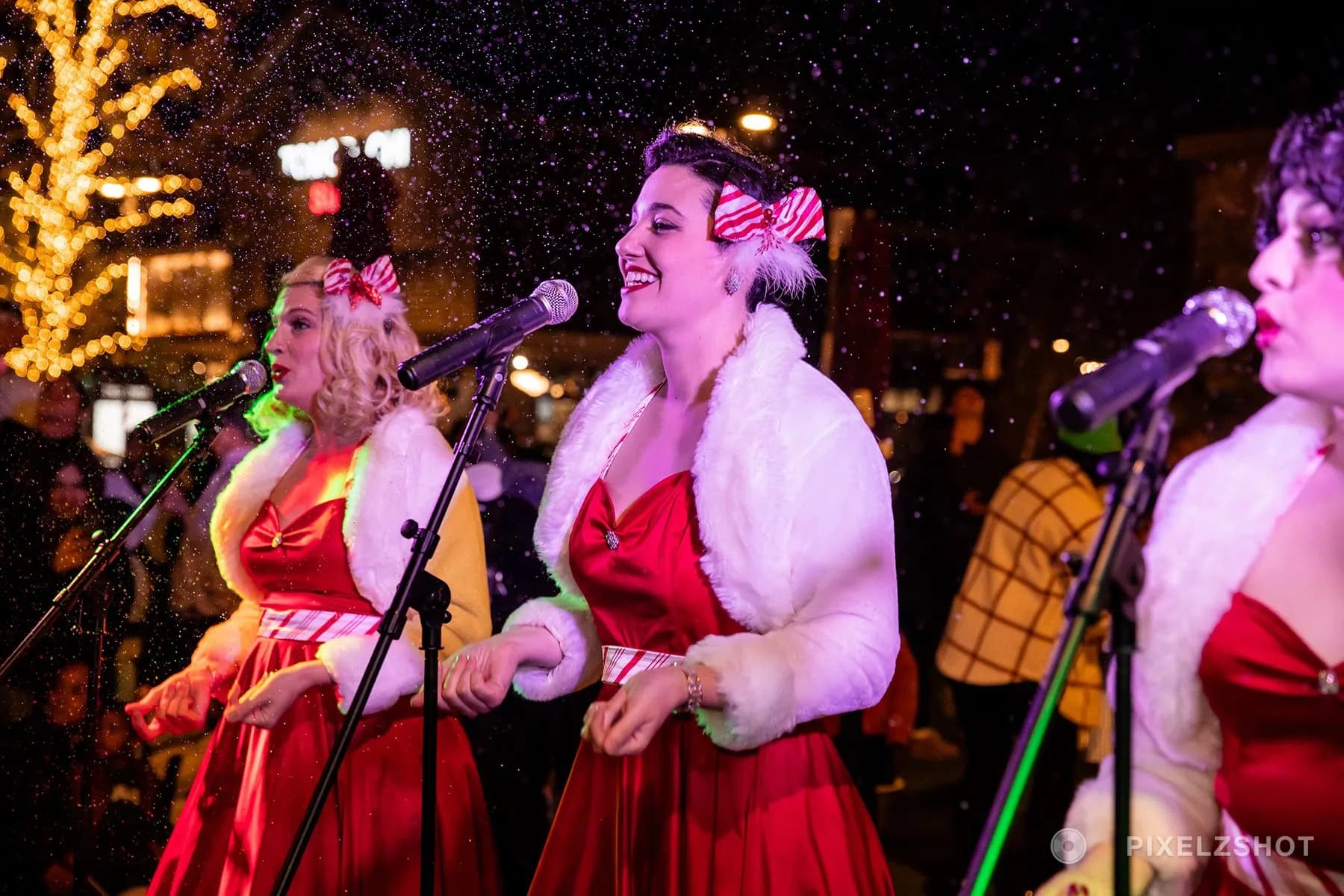 The carolers mid-song with machine snow falling through the stage lights around them