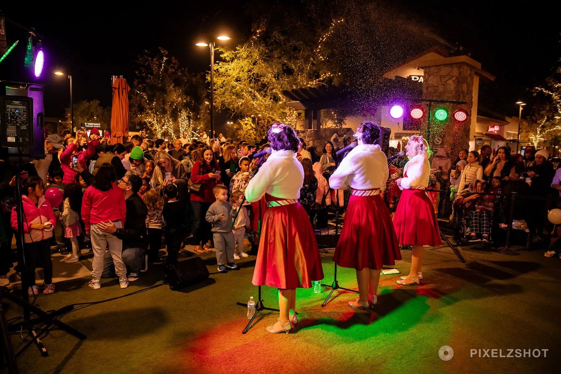 The carolers from behind, facing a plaza packed with families watching and filming on their phones