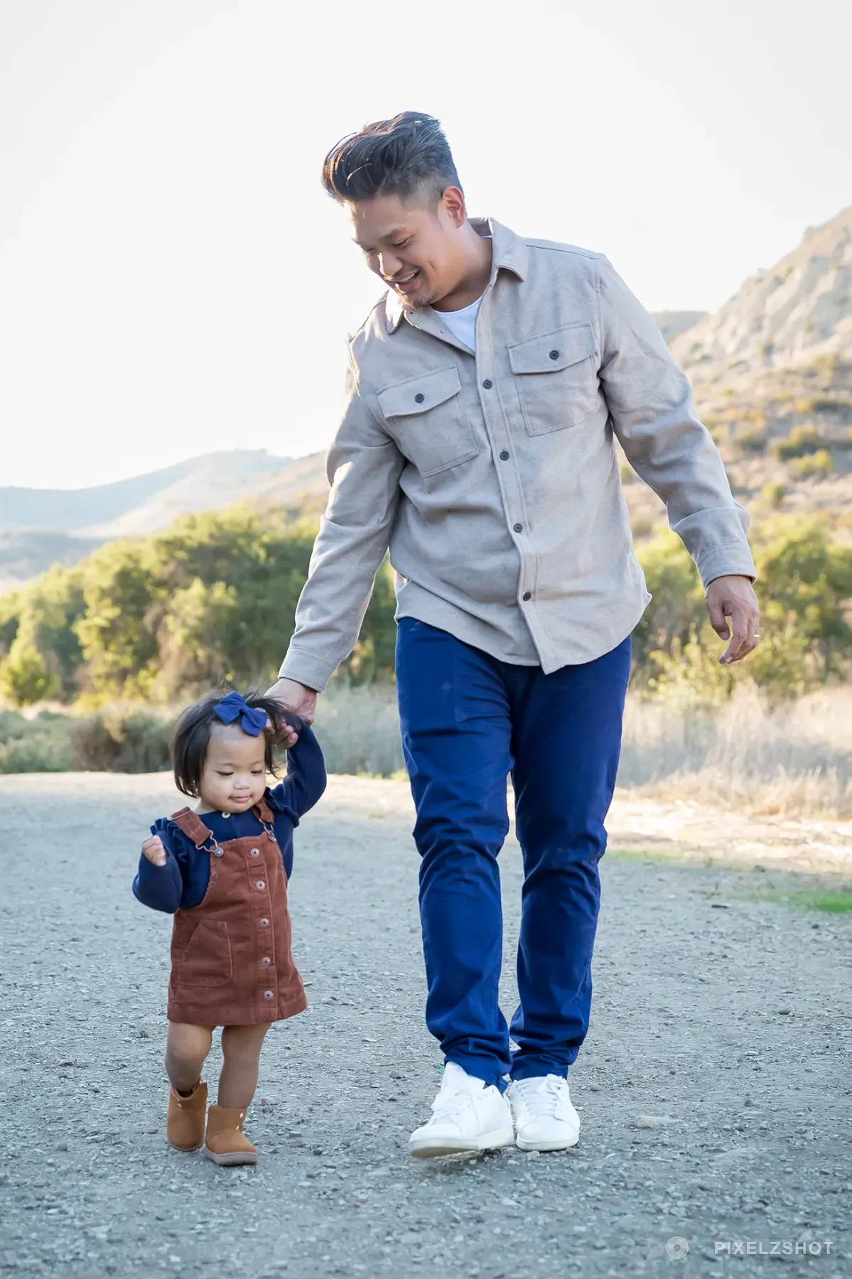 The youngest walking down a gravel canyon path with one hand up in her father's, both of them looking at her feet