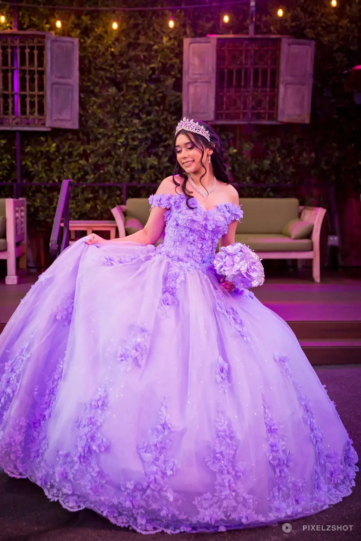Jasmine in a lilac floral ballgown and tiara, holding the skirt out wide on the string-lit courtyard patio