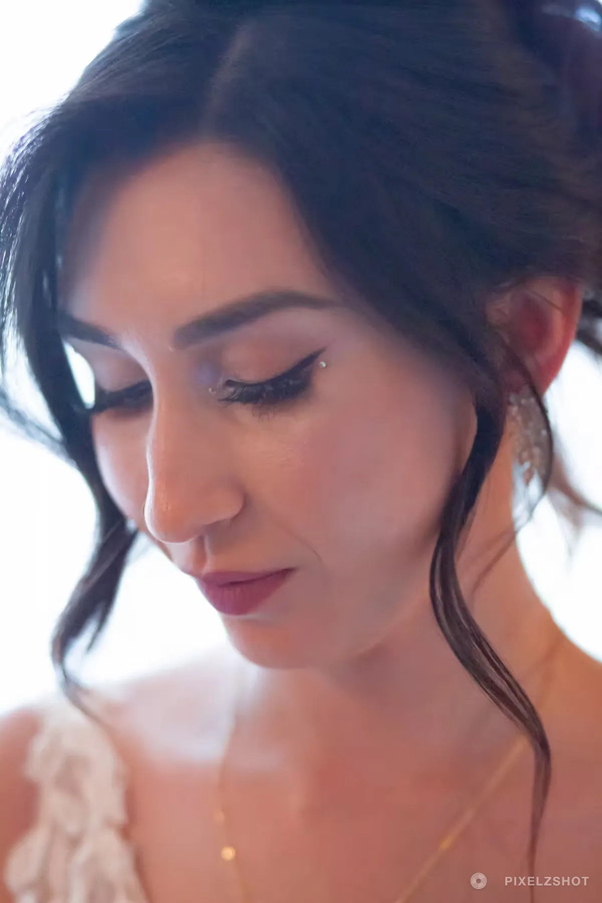 Close bridal portrait in soft window light, hair up with loose strands and a crystal earring