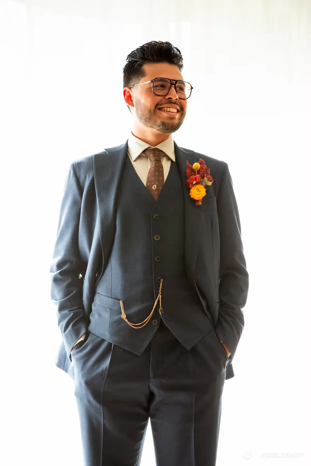 Portrait in a navy three-piece suit with a gold watch chain and a boutonniere of orange and red blooms