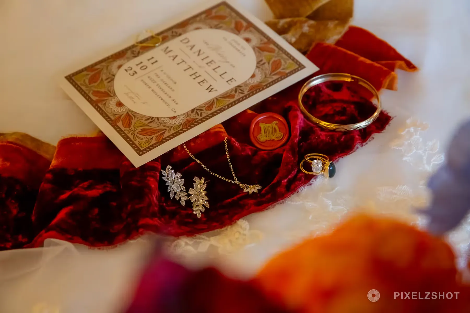 Crystal earrings, a gold necklace, a bangle and an emerald ring set on red velvet beside the invitation and a wax seal