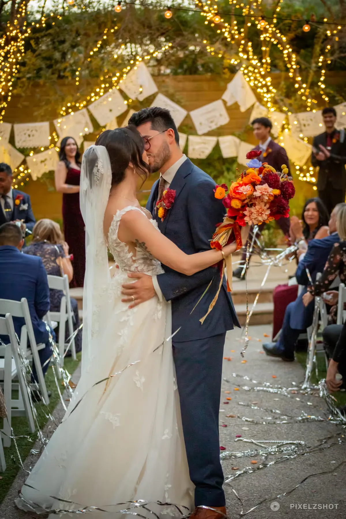 Danielle and Matthew holding each other in the aisle among silver streamers, the bouquet of orange and red blooms raised
