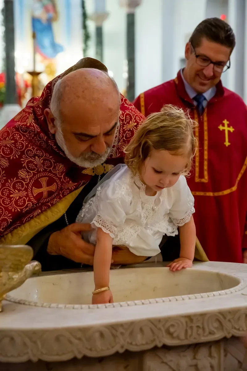 Priest blessing a young child at the baptismal font during a christening ceremony