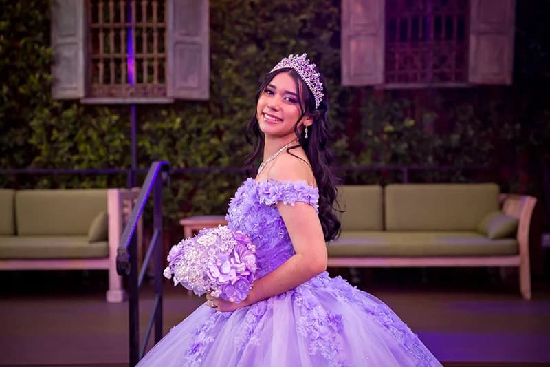 Quinceañera in a lavender gown and tiara smiling while holding her bouquet