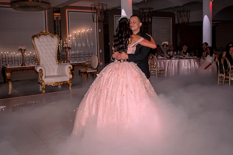 Quinceañera dancing with her father on a fog-covered floor during the reception