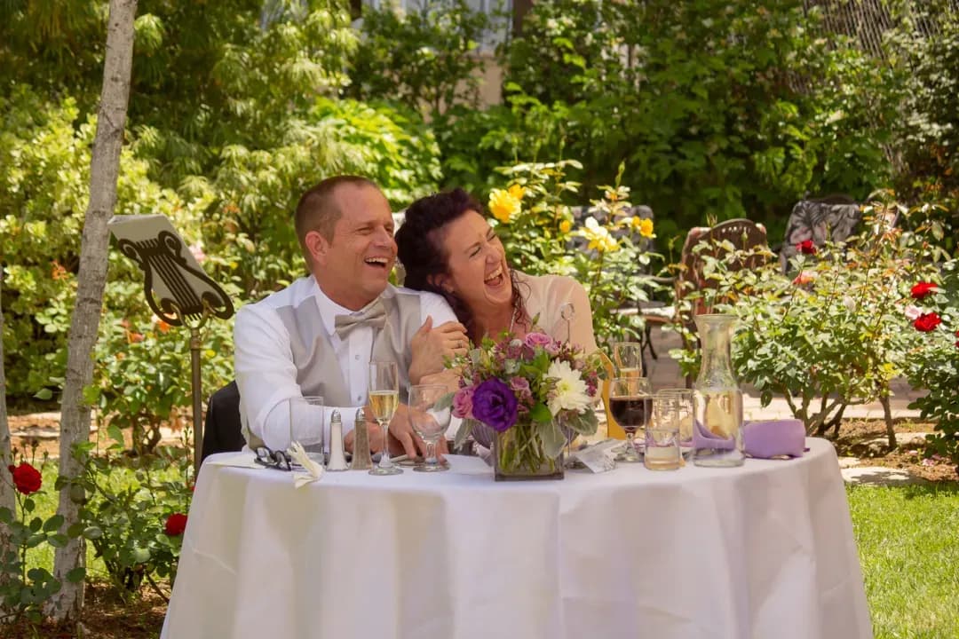 Newlyweds laughing together at their sweetheart table during the reception