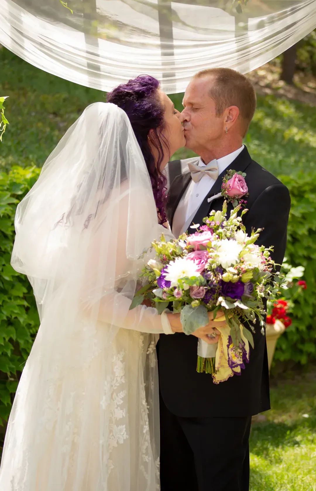 Bride and groom sharing a kiss beneath a sheer canopy at their ceremony